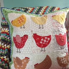 a pillow with chickens on it sitting next to a chair and pillows in the background