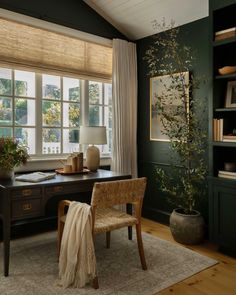 a room with a desk, chair and large window in the corner that has curtains on it