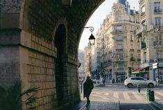 a man walking down a street next to tall buildings and parked cars in front of them