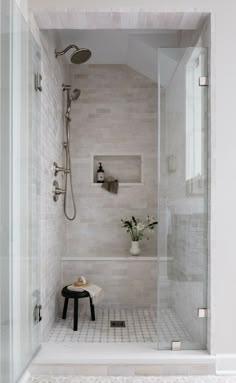 a walk in shower sitting next to a white tiled wall and floor with a bench