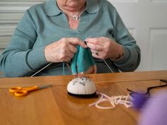 an older woman is working on something with yarn and scissors in front of her sitting at a table