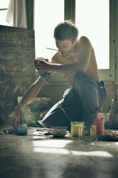 a shirtless man sitting on the floor painting