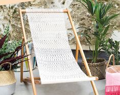 a white lawn chair sitting next to some potted plants and a pink lamp on top of a wooden stand