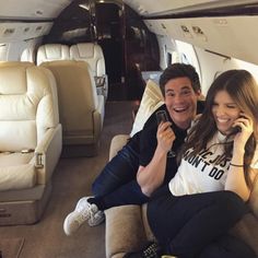 a man and woman sitting on the back of an airplane while talking on their cell phones