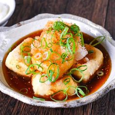 a white bowl filled with fish covered in sauce and garnished with scallions