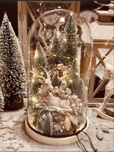 a snow globe filled with christmas decorations and lights on top of a table next to small trees