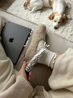 a dog laying on the floor next to a person holding an apple laptop and a pillow