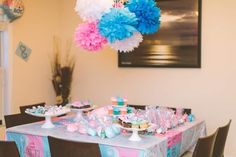 the table is decorated with blue, pink and white pom poms hanging from the ceiling