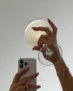 two women holding wine glasses and cell phones with their hands reaching for the same glass