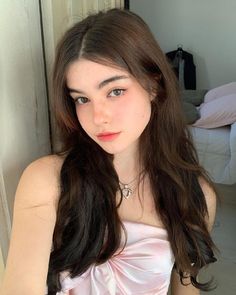 a young woman with long brown hair wearing a pink dress and posing for the camera