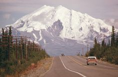 an old car driving down the road in front of a snow covered mountain