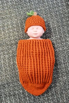 a crocheted baby doll is laying on the floor wearing an orange knitted hat