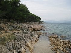 an empty beach with rocks and trees on the shore, along which there is a body of water