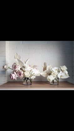 three vases filled with flowers sitting on top of a wooden table next to a brick wall