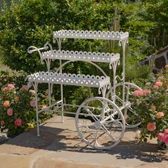 a white metal carriage sitting on top of a stone walkway next to flowers and bushes