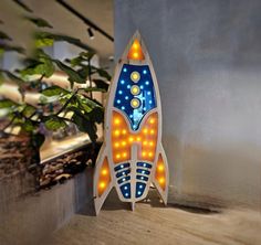 a light up rocket ship sitting on top of a wooden table next to a potted plant