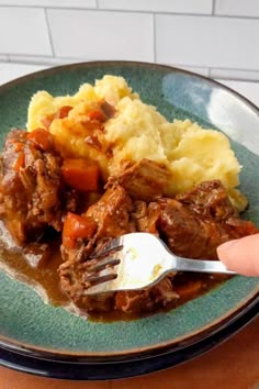 a plate with meat and mashed potatoes on it, being held by a fork