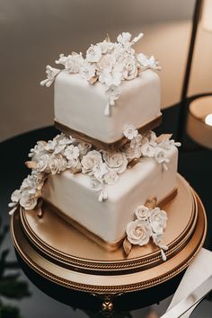 two tiered cake with white flowers on top sitting on a table next to a lit candle