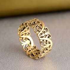 an intricately designed gold ring sits on a gray surface in front of a yellow background