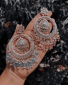 a woman's hand holding two pairs of diamond and pearl earrings in front of a black background