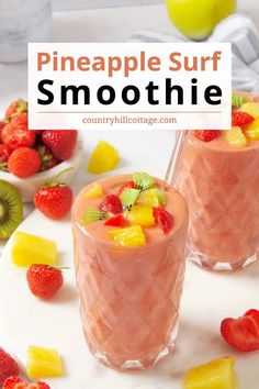 two glasses filled with smoothie and topped with pineapple, kiwi and strawberries