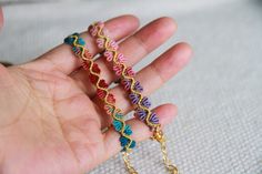 the hand is holding three colorful bracelets on it's fingers, and one has a chain attached to it