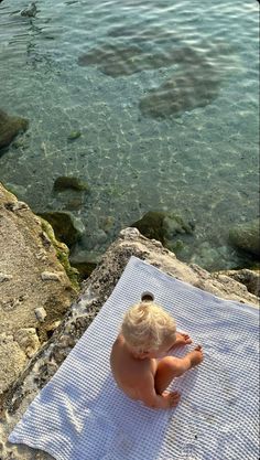 a little boy sitting on top of a towel near the water