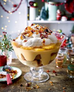 a dessert dish with whipped cream, fruit and nuts in it on a wooden table