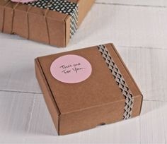 two brown boxes with pink and black bows on them, one has a thank you sticker