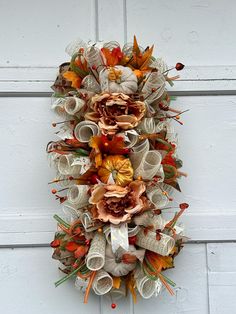 a wreath made out of books and paper flowers hanging on a white door with autumn leaves