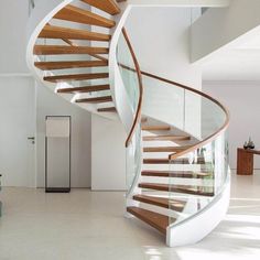 there is a spiral staircase in the middle of this room with glass railings and wood handrails