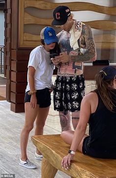 three people sitting on a wooden bench looking at their cell phones in front of them