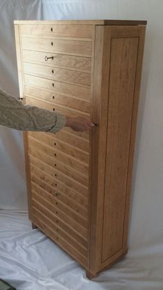 a person is reaching into a large wooden cabinet that has drawers on the front and sides