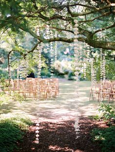 an outdoor ceremony set up with wooden chairs and flowers hanging from the trees in front of it