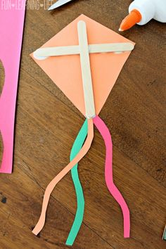 a paper kite sitting on top of a wooden table next to scissors and glue stick