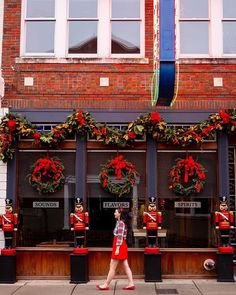 a woman walking down the street in front of a building with christmas wreaths on it