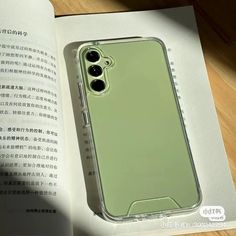 an open book with a green case sitting on top of it next to a cell phone