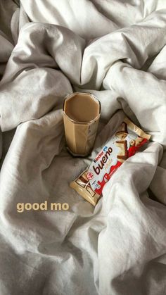 a cup of coffee sitting on top of a bed next to a bag of chips