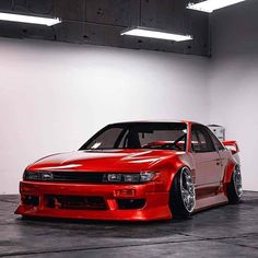 a red car parked in a garage next to a white wall with lights on it