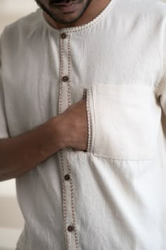 This Dawning Layered Shirt comes in a calm and soothing color. This layered shirt with an interesting play of panelling of two fabrics, Kala Cotton and self-checked, is undyed and unbleached. Replete with a classic round neck, this half-sleeve shirt comes with two functional pockets. Stitches of Kantha, a form of Indian hand embroidery, line the placket, neckline and pockets. *This item is a final sale and not eligible for returns or exchanges. *This item can take up to 14 business days to ship Men Embroidery Shirts, Shirt Pocket Embroidery, Men Shirt Design, Mens Shirt Details, Indian Hand Embroidery, Linen Kurti, Embroidery Shirt Men, Menswear Details, Stylish Shirts Men