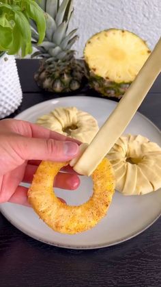 someone is cutting up some pineapple slices on a white plate with a large knife