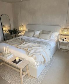 a white bed sitting in a bedroom next to two tables with candles on top of it