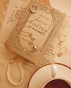 an antique book, bracelets and ring are on the table next to a cup of coffee