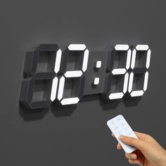 a person holding a remote in front of a digital clock