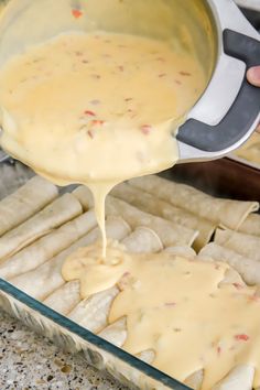 someone pouring cheese sauce on some pita bread in a baking pan with other food items