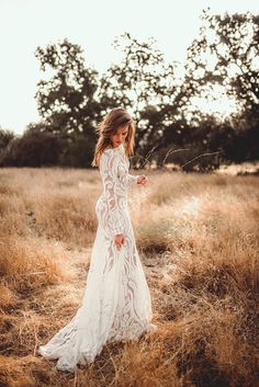 a woman in a long white dress standing in the middle of a field with tall grass