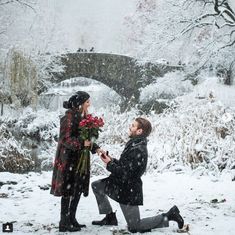 a man kneeling down next to a woman with flowers on her lap in the snow