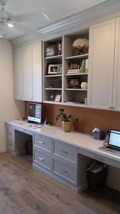 a desk with a laptop on top of it in front of white cabinets and drawers