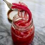 a jar filled with red liquid sitting on top of a table next to a spoon