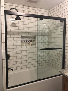 a white tiled bathroom with black trim and glass shower door that opens up to the bathtub